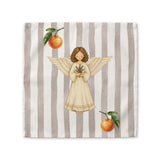 Angels and oranges Christmas cloth napkin laid flat, showing the angel and pine sprig on a soft grey stripe with oranges beside it