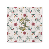 Poinsettia and olive Christmas cloth napkin laid flat, showing poinsettias, red holly berries, gold pine cones and olive branches on cream