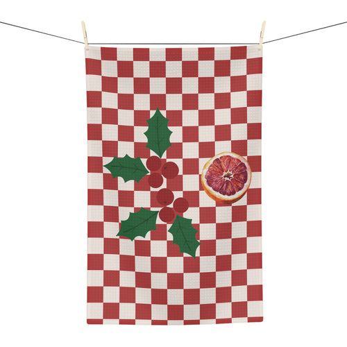 Blood orange check Christmas tea towel hanging from a line, a red and cream checkerboard with a sprig of holly and a cut blood orange