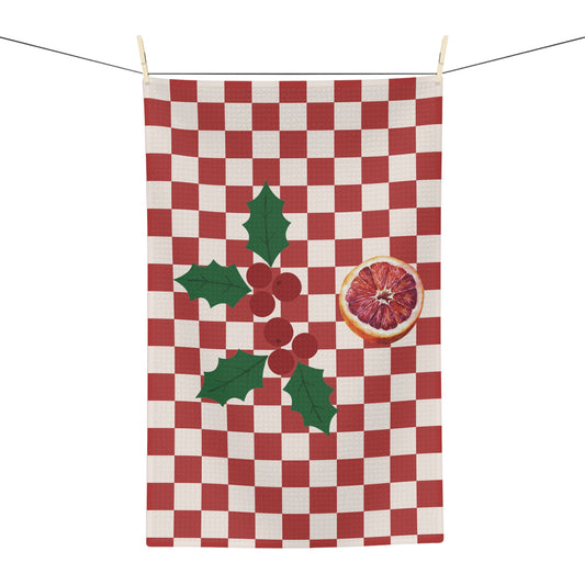 Blood orange check Christmas tea towel hanging from a line, a red and cream checkerboard with a sprig of holly and a cut blood orange
