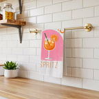 Aperitivo Spritz tea towel hanging from a brass rail against white subway tile