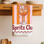 Spritz Club tea towel folded over a wooden shelf rail above a kitchen counter