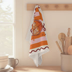 Spritz Club tea towel hanging from a peg rail beside a window, with wooden utensils and stacked bowls