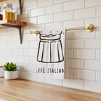 Caffè Italiano tea towel hanging from a brass rail against white subway tile