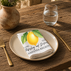 Limoncello napkin on a cream plate with a glass of water and a terracotta vase of Mediterranean wildflowers on rustic wood