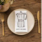 Caffè Italiano napkin folded on a cream plate between gold cutlery, beside a terracotta vase of Mediterranean wildflowers
