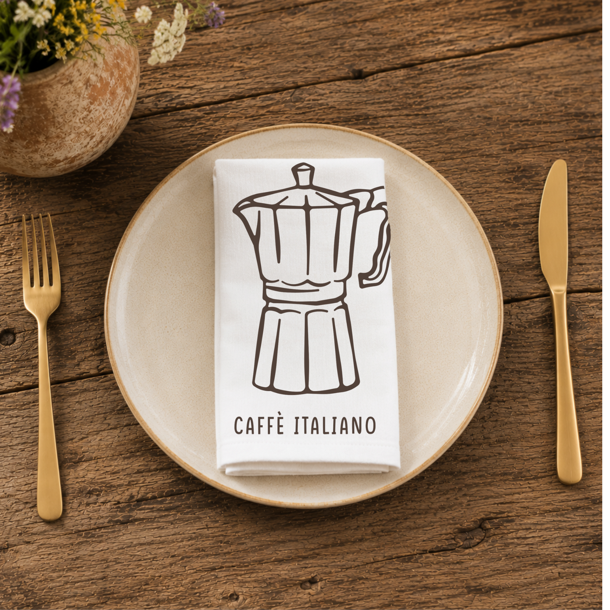 Caffè Italiano napkin folded on a cream plate between gold cutlery, beside a terracotta vase of Mediterranean wildflowers