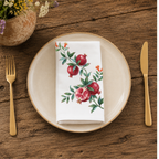 Pomegranate napkin folded on a cream plate between gold cutlery, beside a terracotta vase of Mediterranean wildflowers