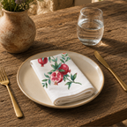 Pomegranate napkin on a cream plate with a glass of water and a terracotta vase of Mediterranean wildflowers