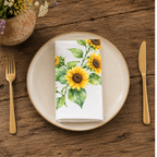 Sunflower napkin folded on a cream plate between gold cutlery, beside a terracotta vase of Mediterranean wildflowers