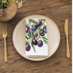 Olive Branch napkin folded on a cream plate between gold cutlery, beside a terracotta vase of Mediterranean wildflowers