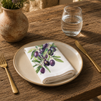 Olive Branch napkin on a cream plate with a glass of water and a terracotta vase of Mediterranean wildflowers