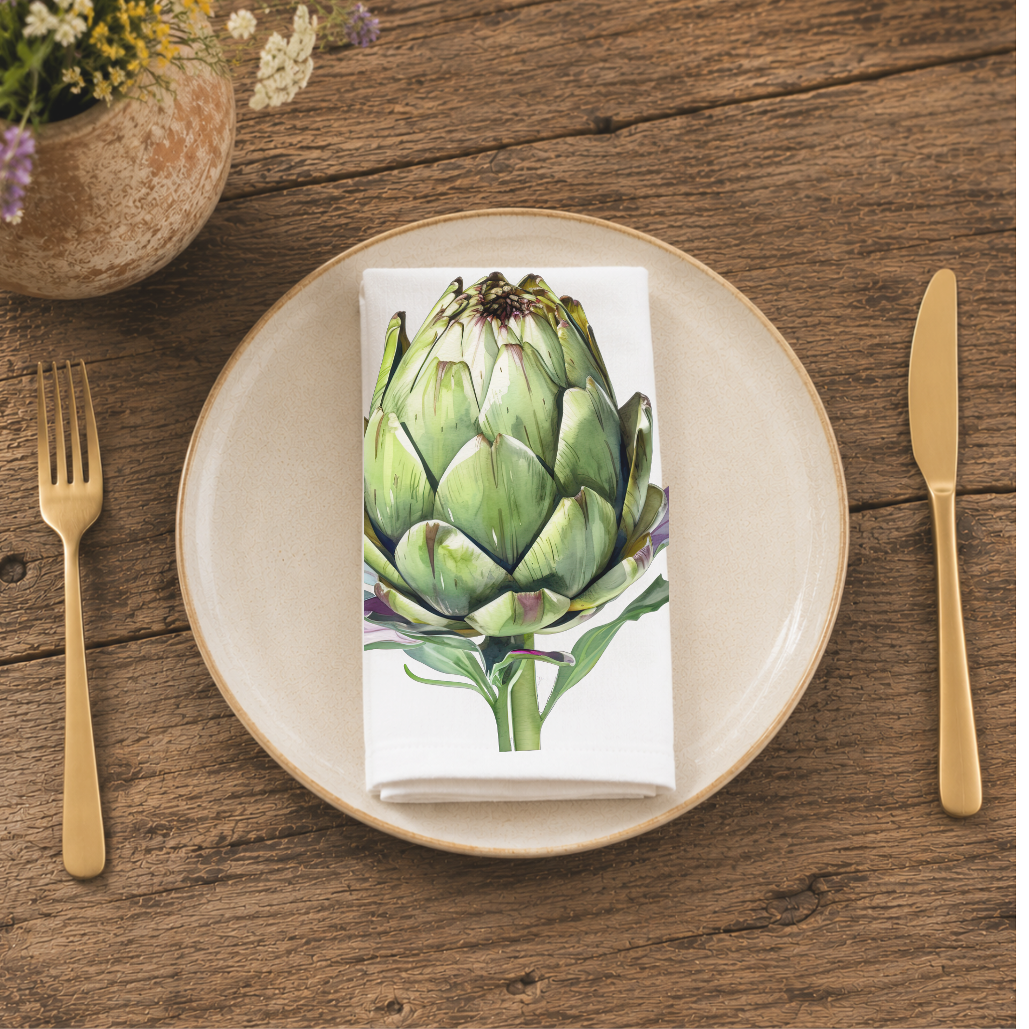 Artichoke napkin folded on a cream plate between gold cutlery, beside a terracotta vase of Mediterranean wildflowers