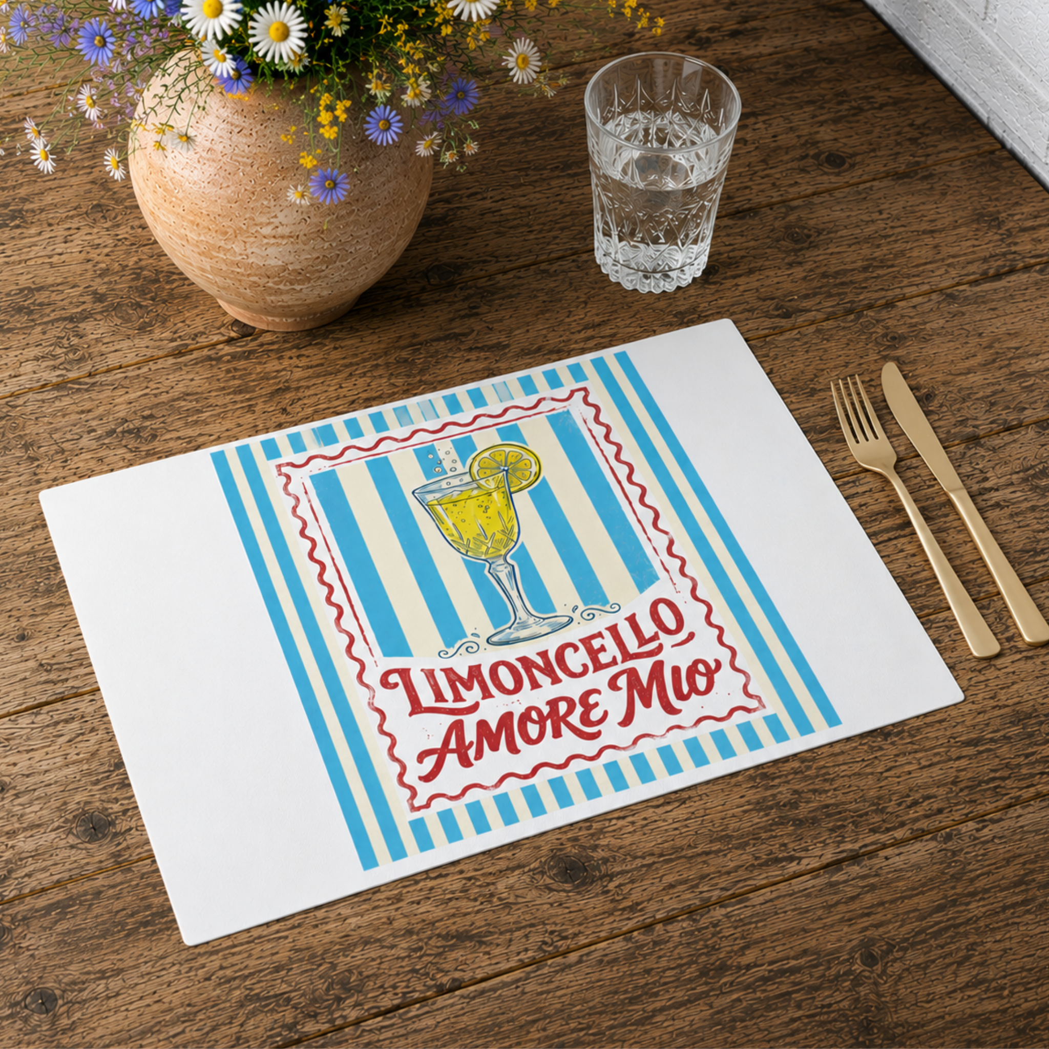 Limoncello Amore Mio placemat on a wooden table with gold cutlery, a glass of water and a terracotta pot of flowers