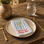 Limoncello Amore Mio napkin on a cream plate with a glass of water and a terracotta vase of Mediterranean wildflowers