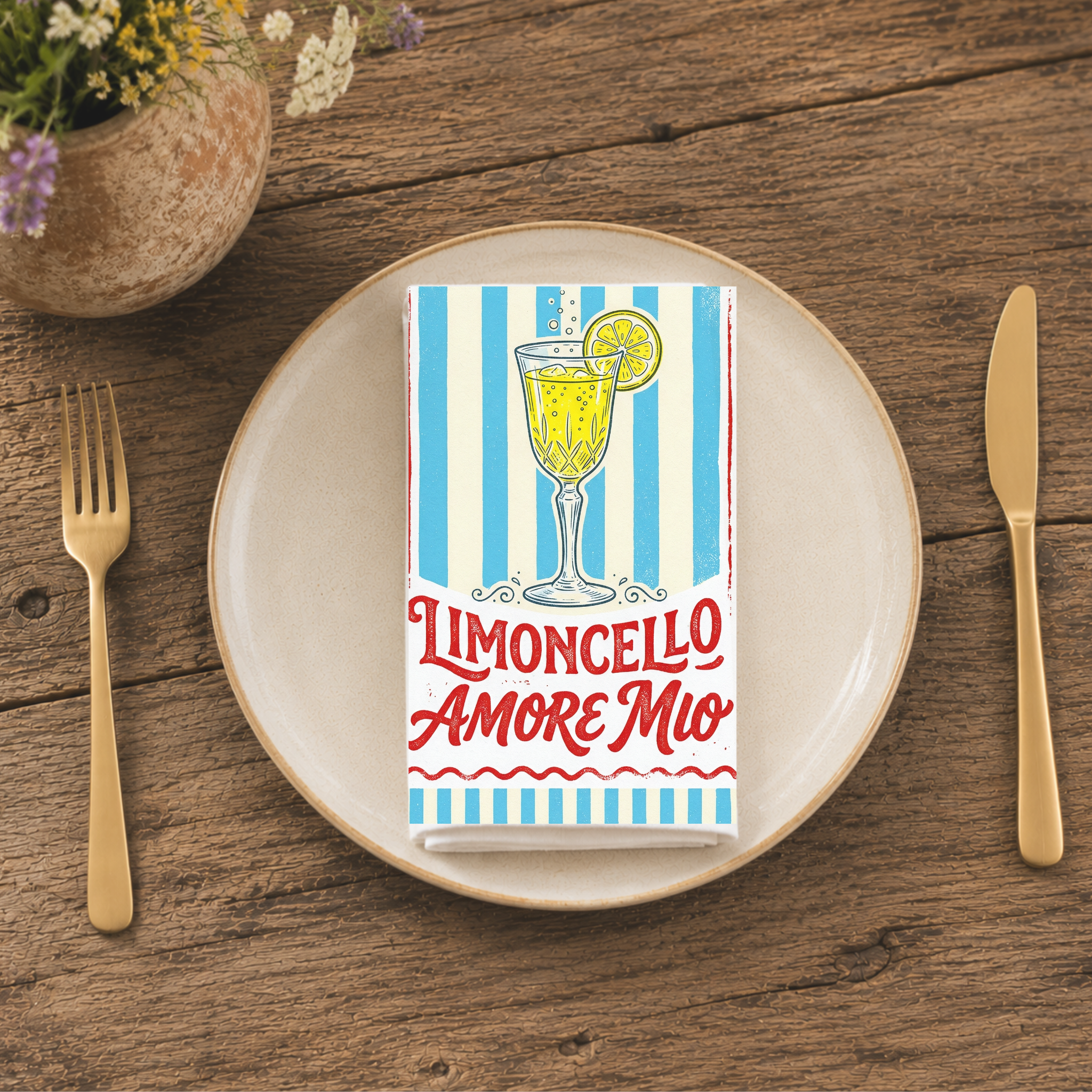 Limoncello Amore Mio napkin folded on a cream plate between gold cutlery, beside a terracotta vase of Mediterranean wildflowers