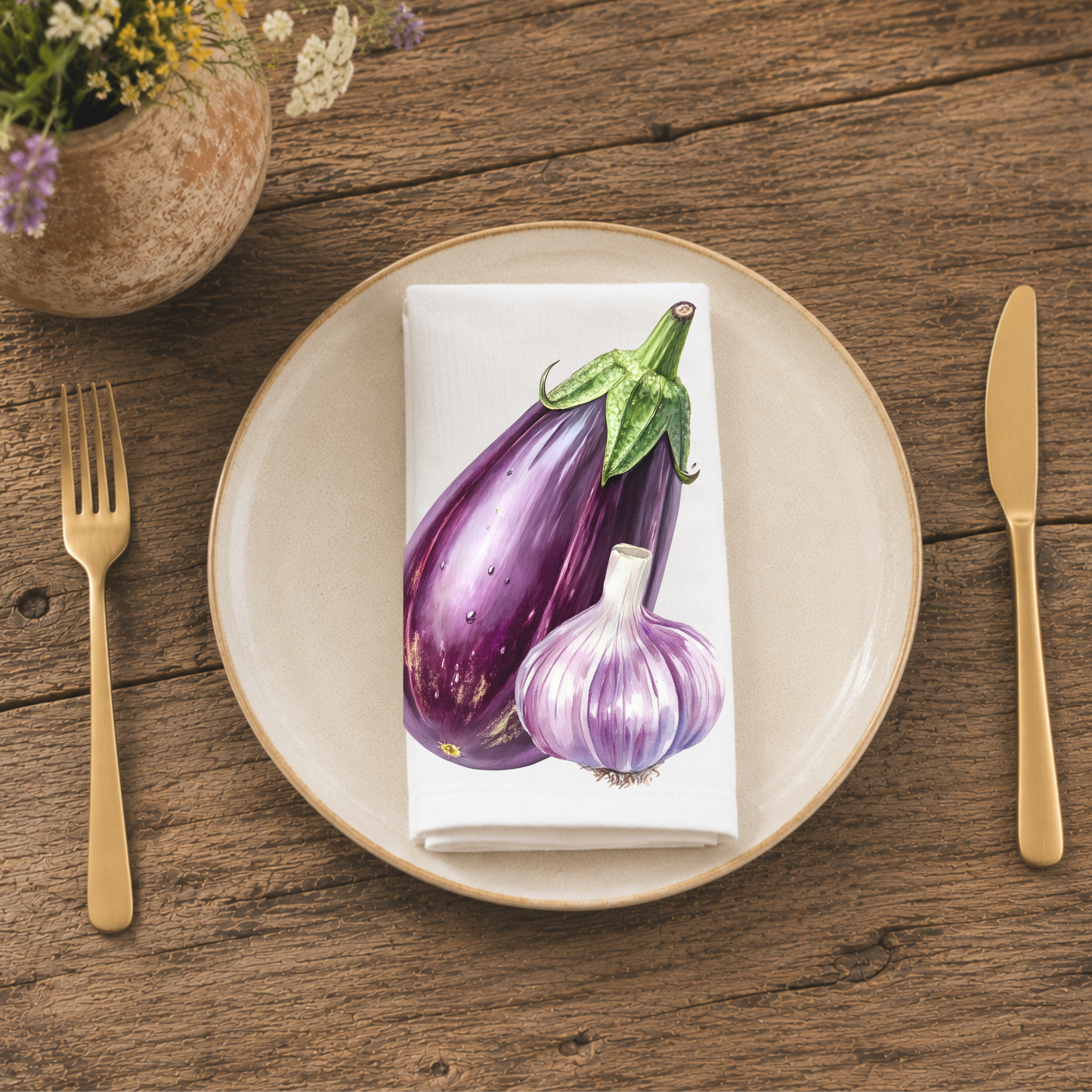 Eggplant and Garlic napkin folded on a cream plate between gold cutlery, beside a terracotta vase of Mediterranean wildflowers