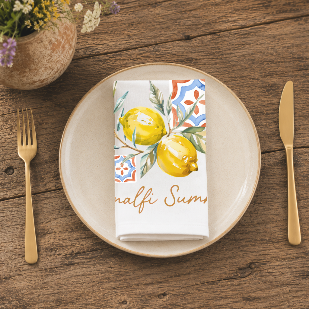 Amalfi Summer napkin folded on a cream plate between gold cutlery, beside a terracotta vase of Mediterranean wildflowers