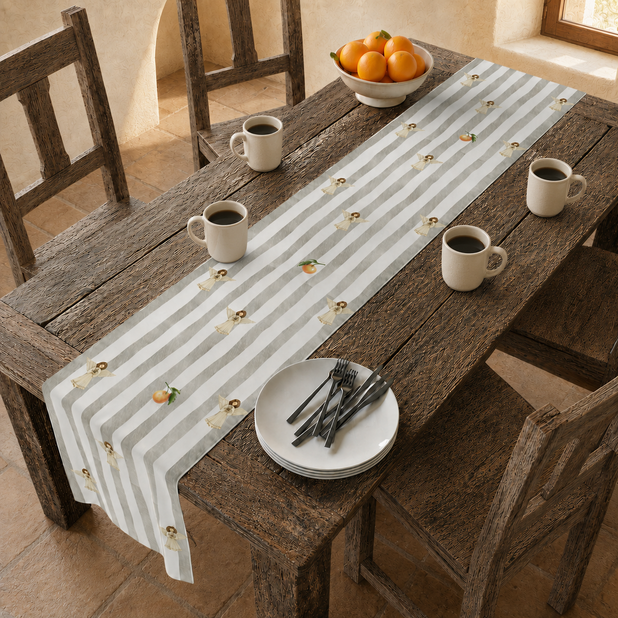 Angels and oranges Christmas table runner down a rustic wooden table, with a bowl of oranges, coffee mugs and stacked plates