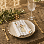 Angels and oranges napkin folded on a stoneware plate in warm sunlight, with gold cutlery and a wine glass
