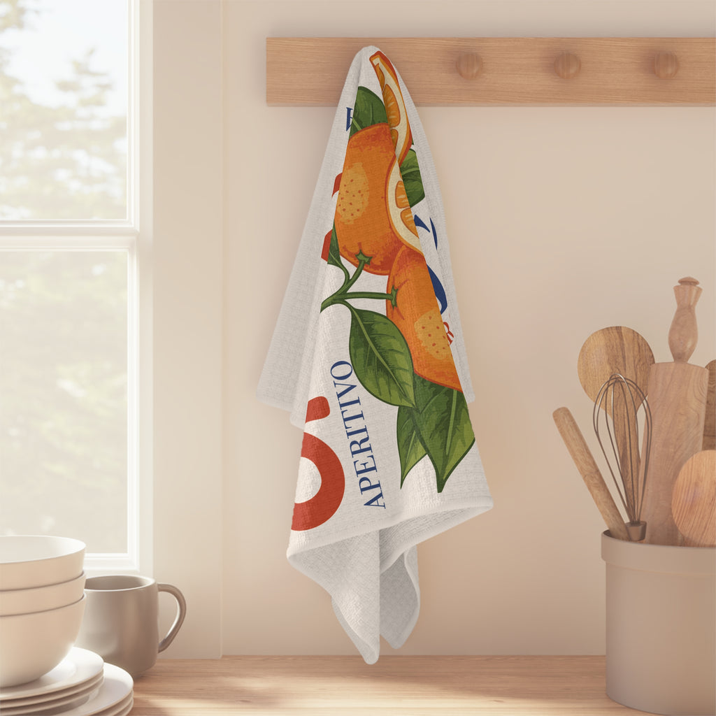 Spritz Veneto tea towel hanging from a wooden peg rail beside a sunlit window, with stacked bowls and a jar of wooden utensils