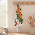 Spritz Veneto tea towel hanging from a wooden peg rail beside a sunlit window, with stacked bowls and a jar of wooden utensils