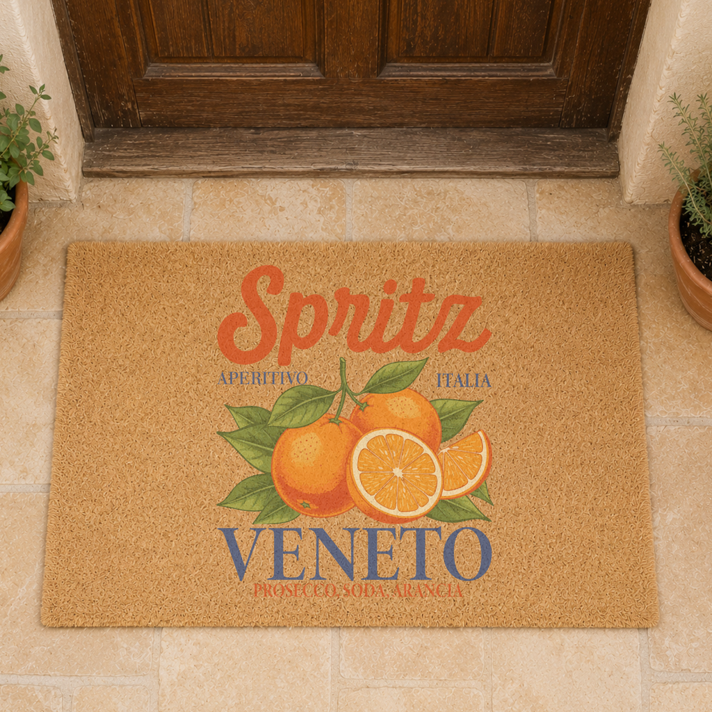 Spritz Veneto coir doormat on stone paving in front of a weathered wooden door, with potted herbs on either side