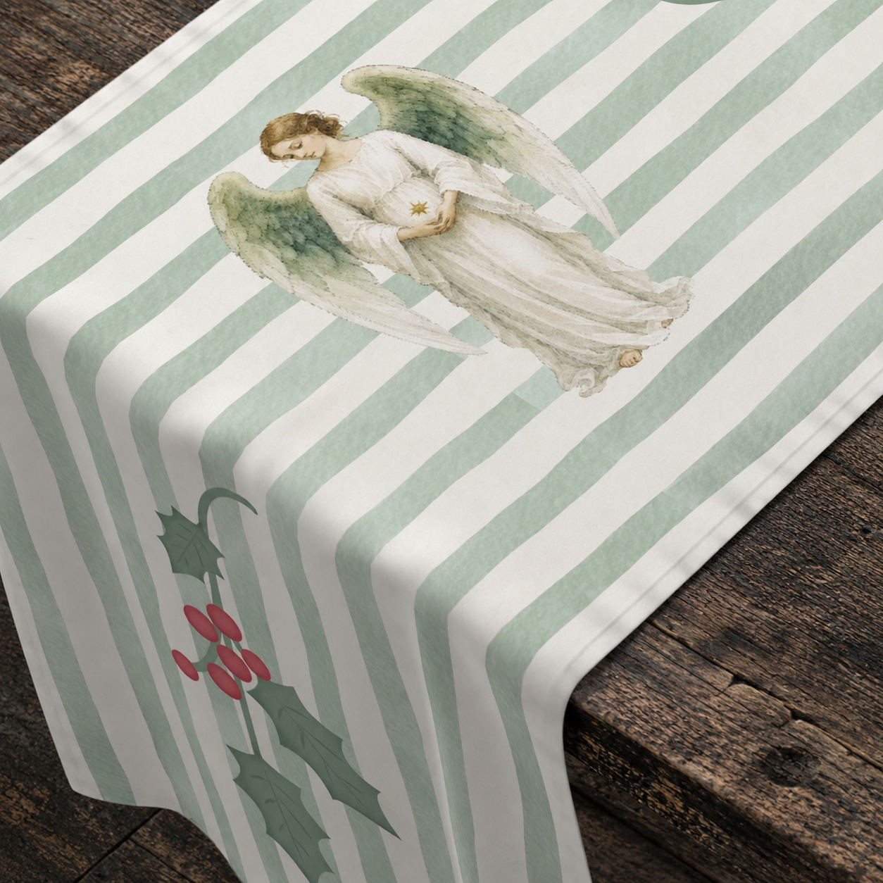 Angels and holly table runner over the corner of a dark wooden table, with an angel turned toward the viewer and holly below
