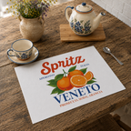 Spritz Veneto placemat on a rustic wooden table with a ceramic cup and saucer, a floral teapot and a vase of wildflowers