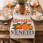 Spritz Veneto table runner running the length of a rustic wooden table set for four, with woven placemats, cream bowls and an olive branch arrangement